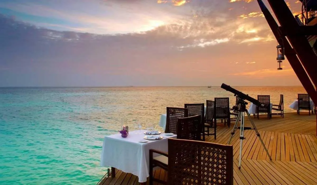 Dining table and telescope on a wooden deck over the sea at sunset