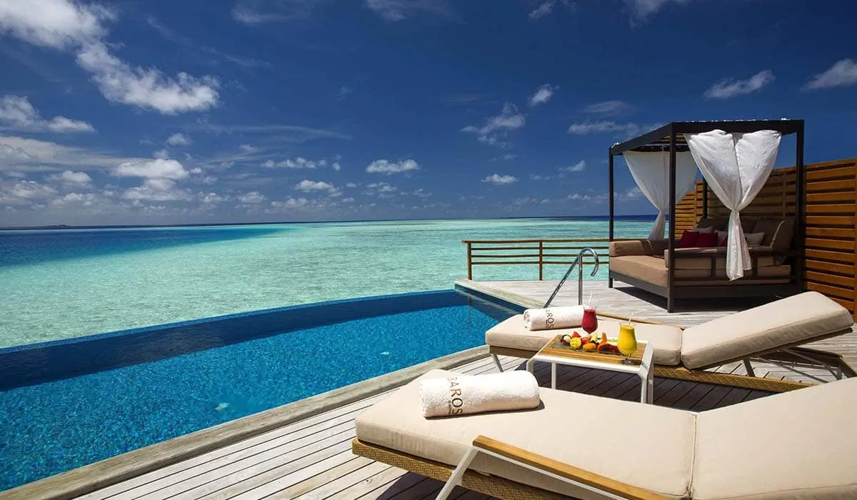 Water villa infinity pool with sun loungers and a curtained daybed above the lagoon
