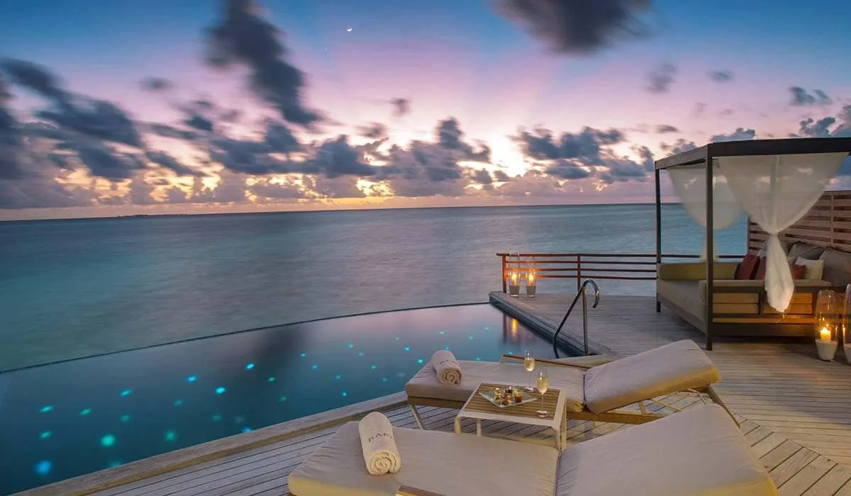 Water villa pool deck with daybed and loungers over the ocean at dusk