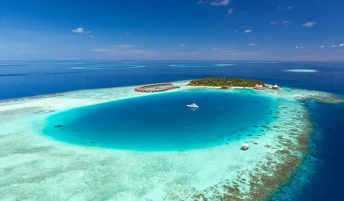 Aerial view of an island resort and water villas beside a deep blue lagoon