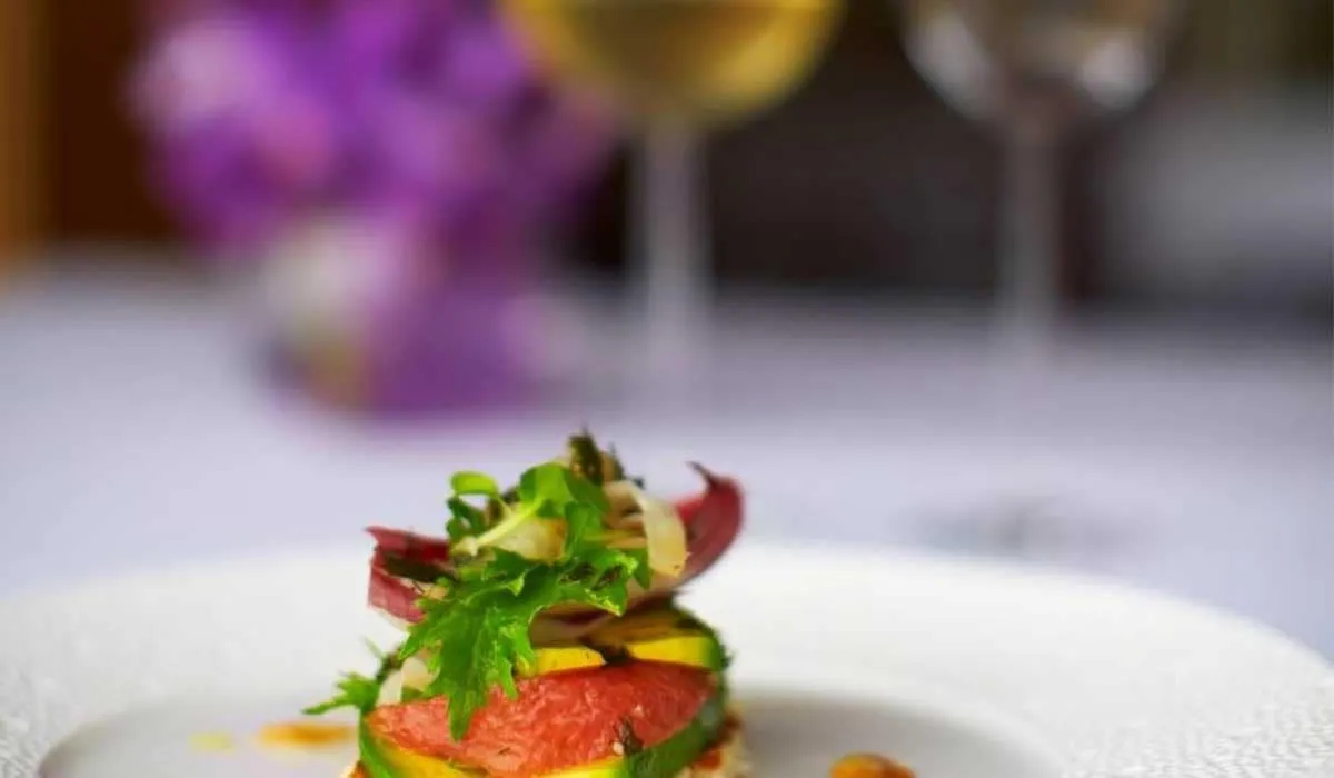 Plated starter with fresh vegetables and garnish, wine glasses behind