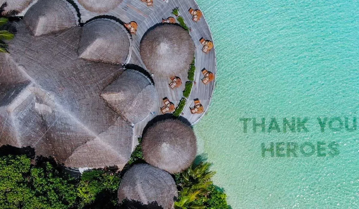 Aerial close-up of thatched roofs beside "Thank you heroes" written in the lagoon