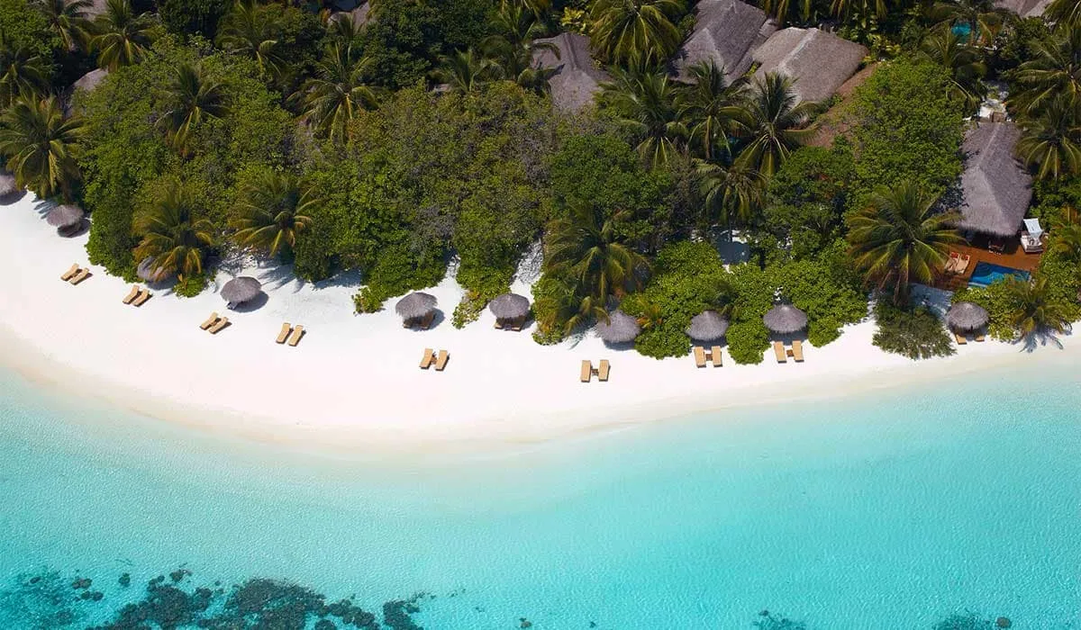Aerial view of the island's white beach lined with sun loungers and palms