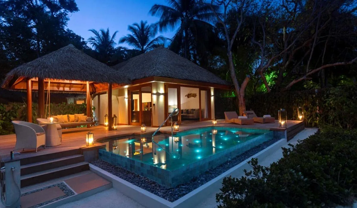 Pool villa with a lit private pool and thatched pavilion at dusk