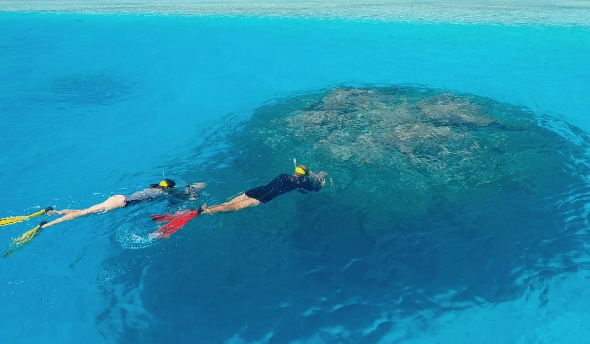 Two snorkellers swimming over a coral outcrop in clear turquoise water