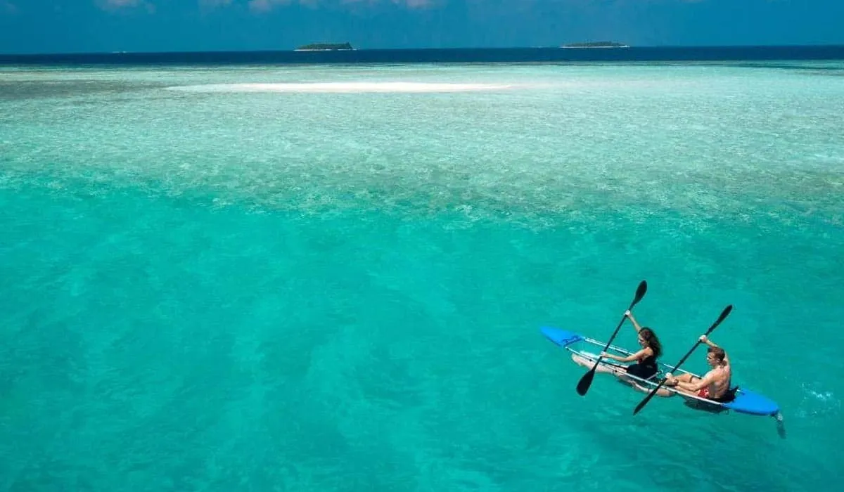 Couple paddling a blue kayak over turquoise shallows