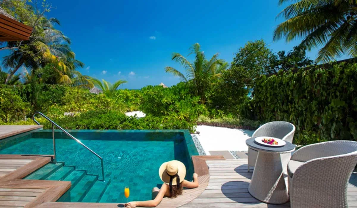 Woman in a sun hat relaxing in a private pool beside a tropical garden