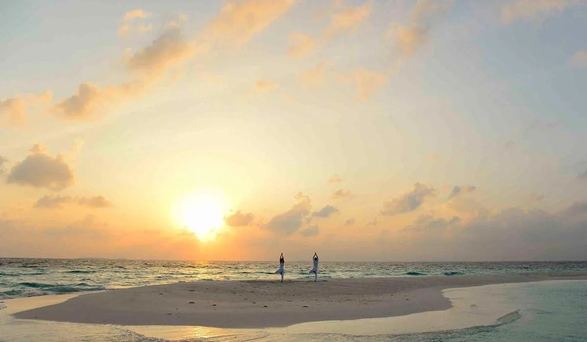 Sun setting over a sandbank, with two people standing at the water's edge