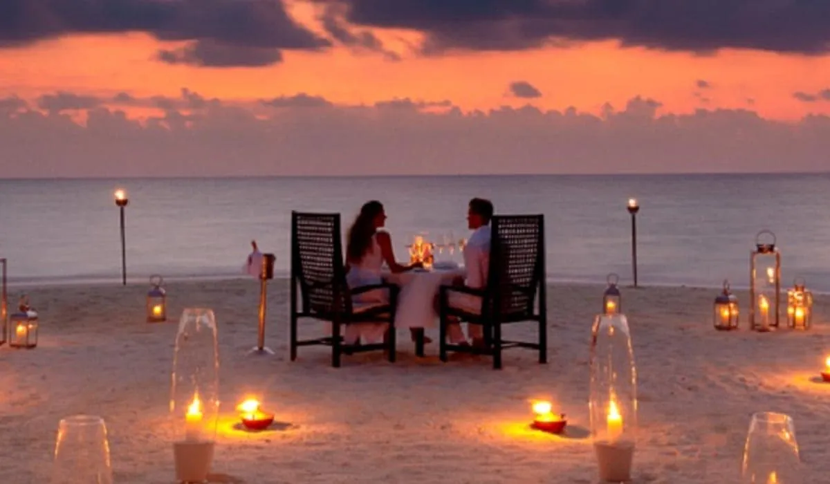 Couple dining by candlelight on the beach at sunset, lit by torches