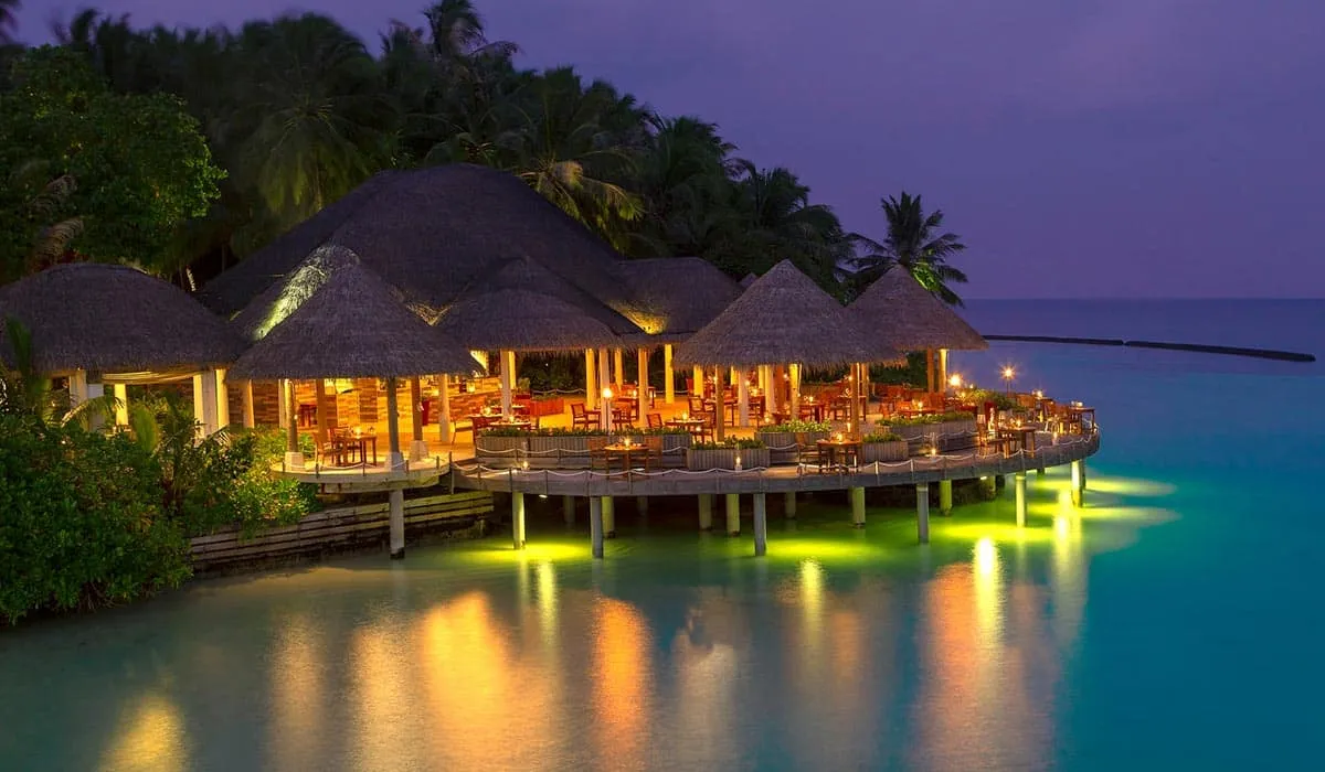 Thatched restaurant over the water lit up at dusk