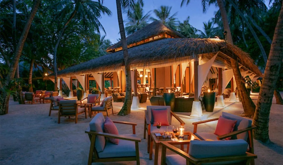 Beach restaurant lit up at dusk, with lounge seating under palms