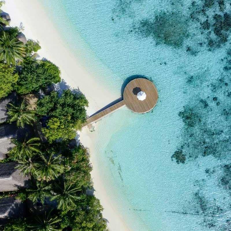 Aerial view of a jetty leading to a round platform off a palm-lined beach