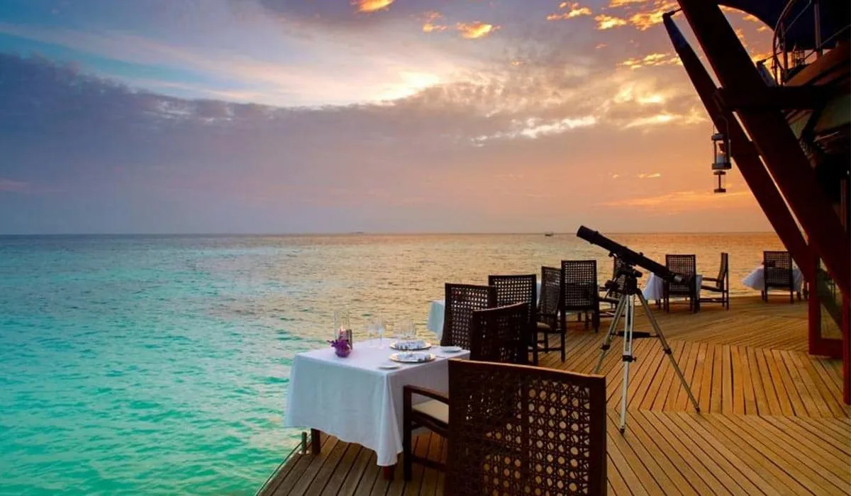 Lighthouse restaurant deck with dining tables and a telescope by the sea at sunset