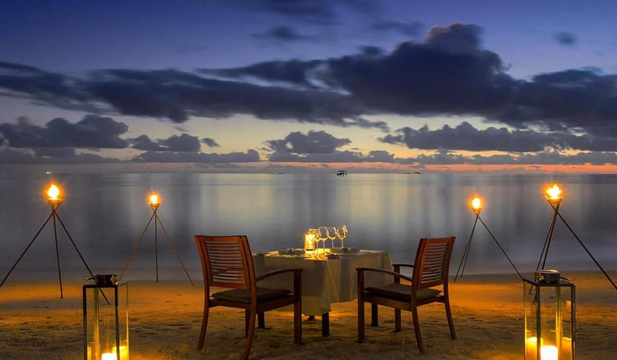 Dinner table for two on the beach lit by torches at dusk