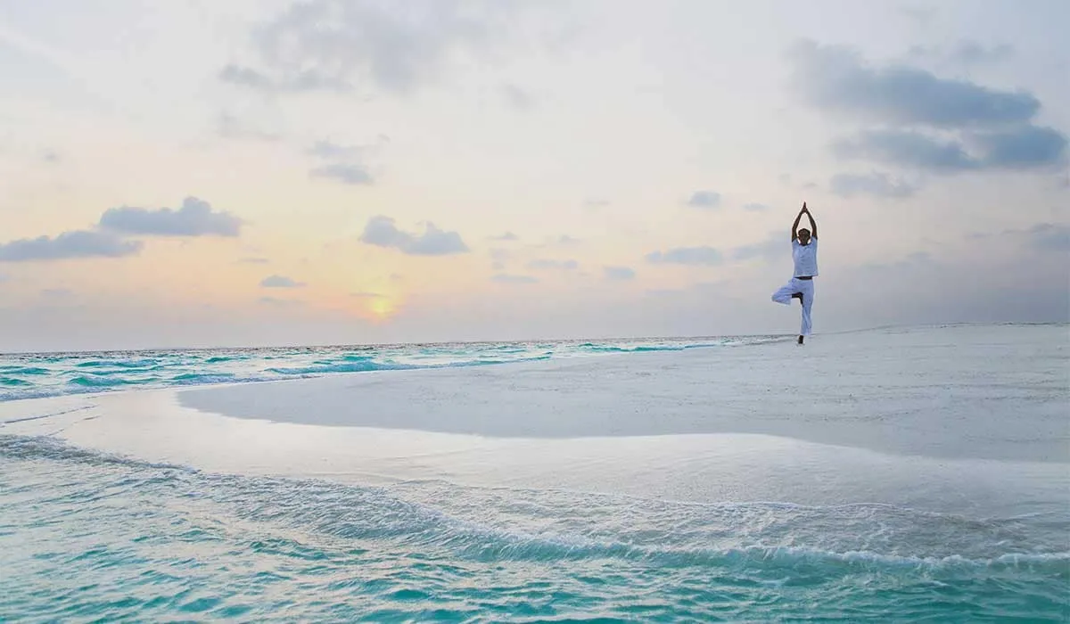 Person in a yoga tree pose on a sandbank at sunrise