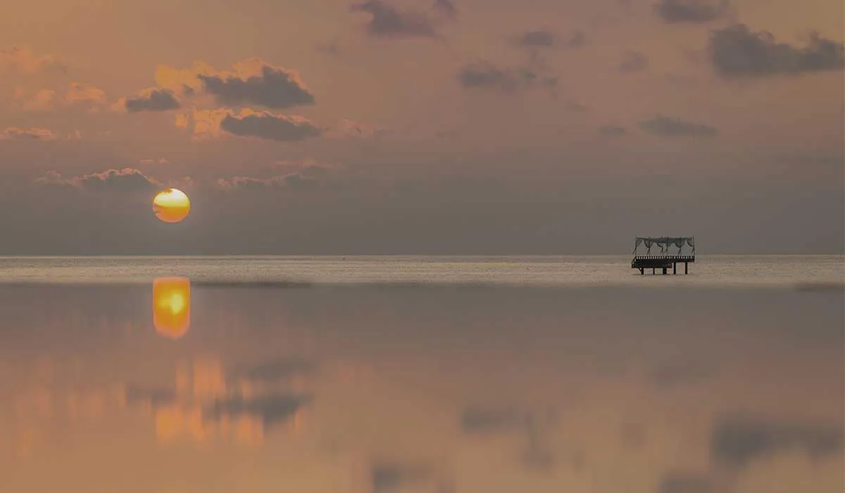 Sun low over a glassy lagoon, with the Piano Deck on the horizon