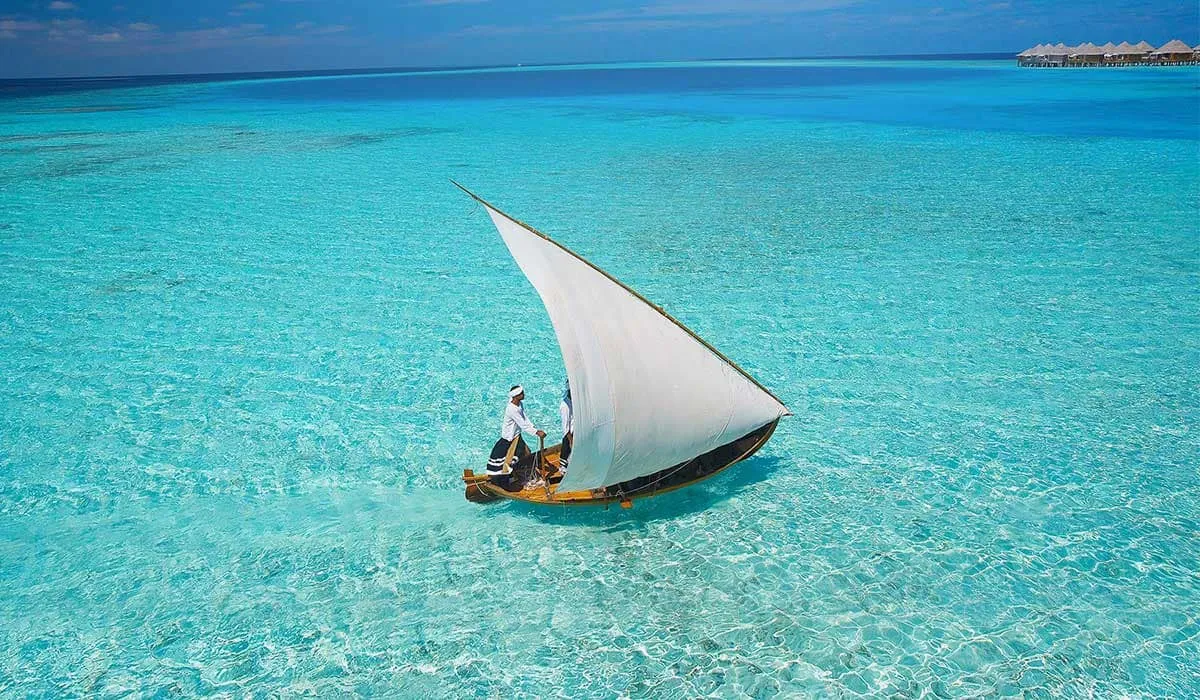 Traditional sailing boat with a white sail on clear turquoise shallows