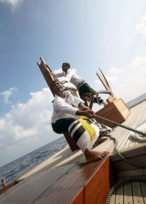 Crew member hauling on a sail line aboard a traditional wooden boat