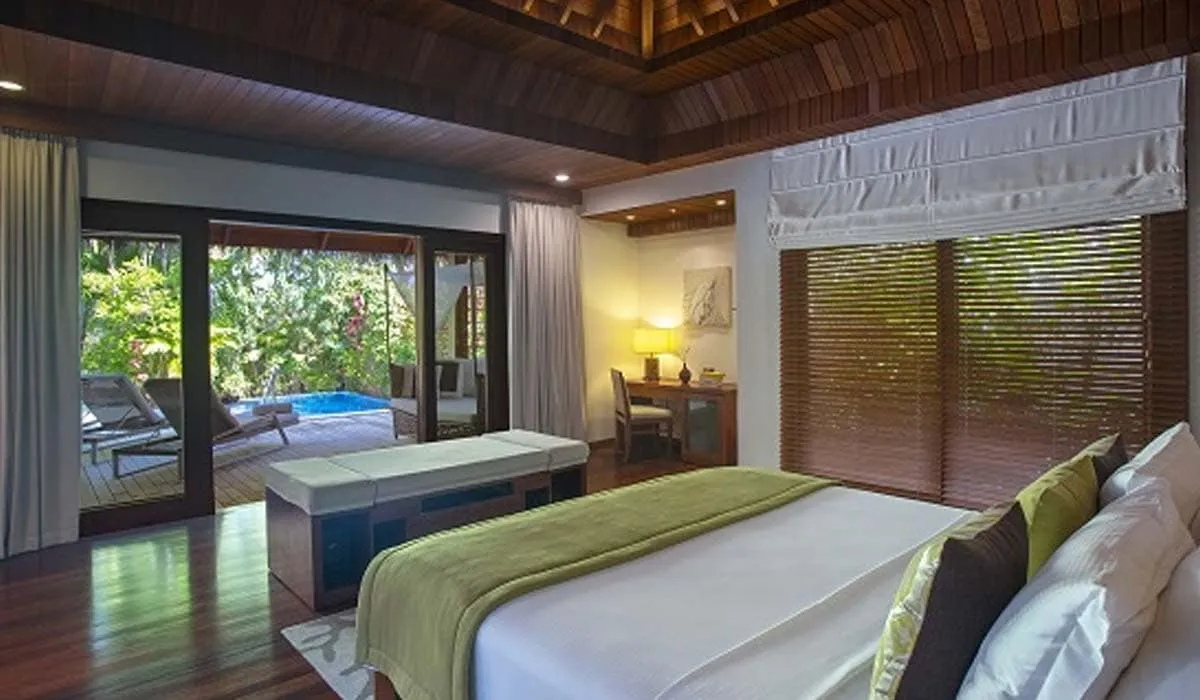 Villa bedroom with a large bed and doors opening to a private pool and garden