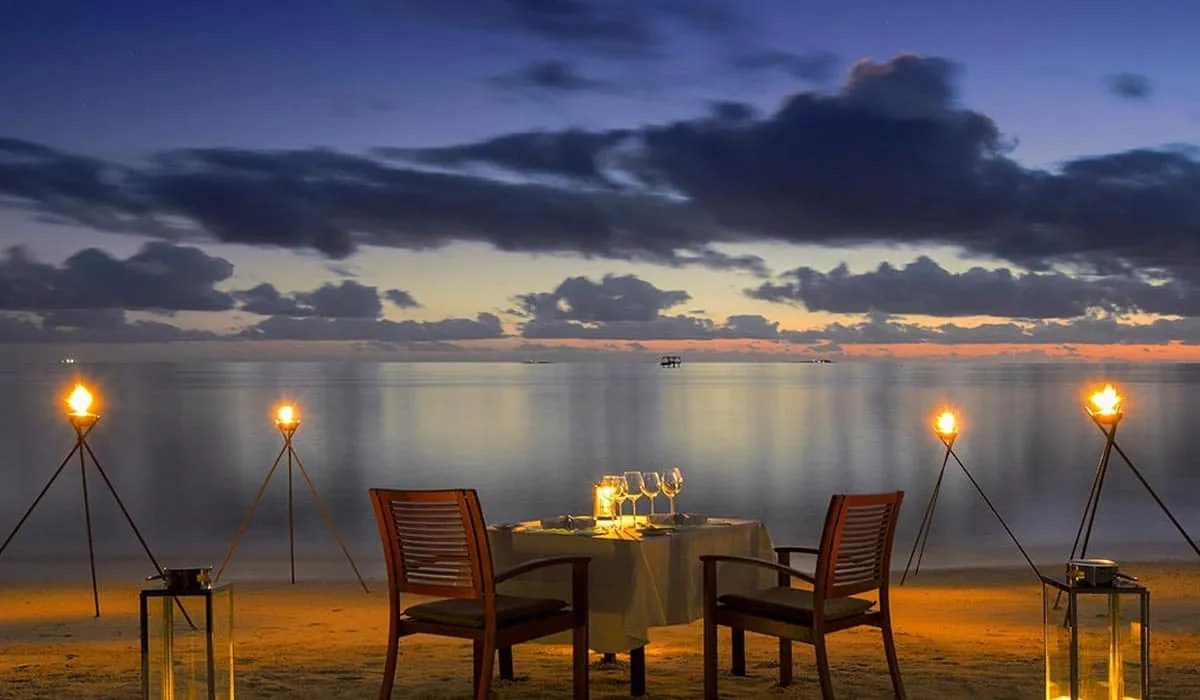 Dinner table for two on the beach lit by torches at dusk