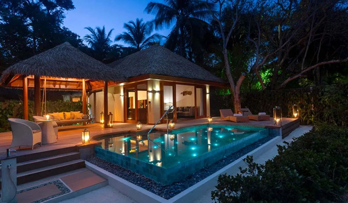Pool villa with a lit private pool and thatched pavilion at dusk