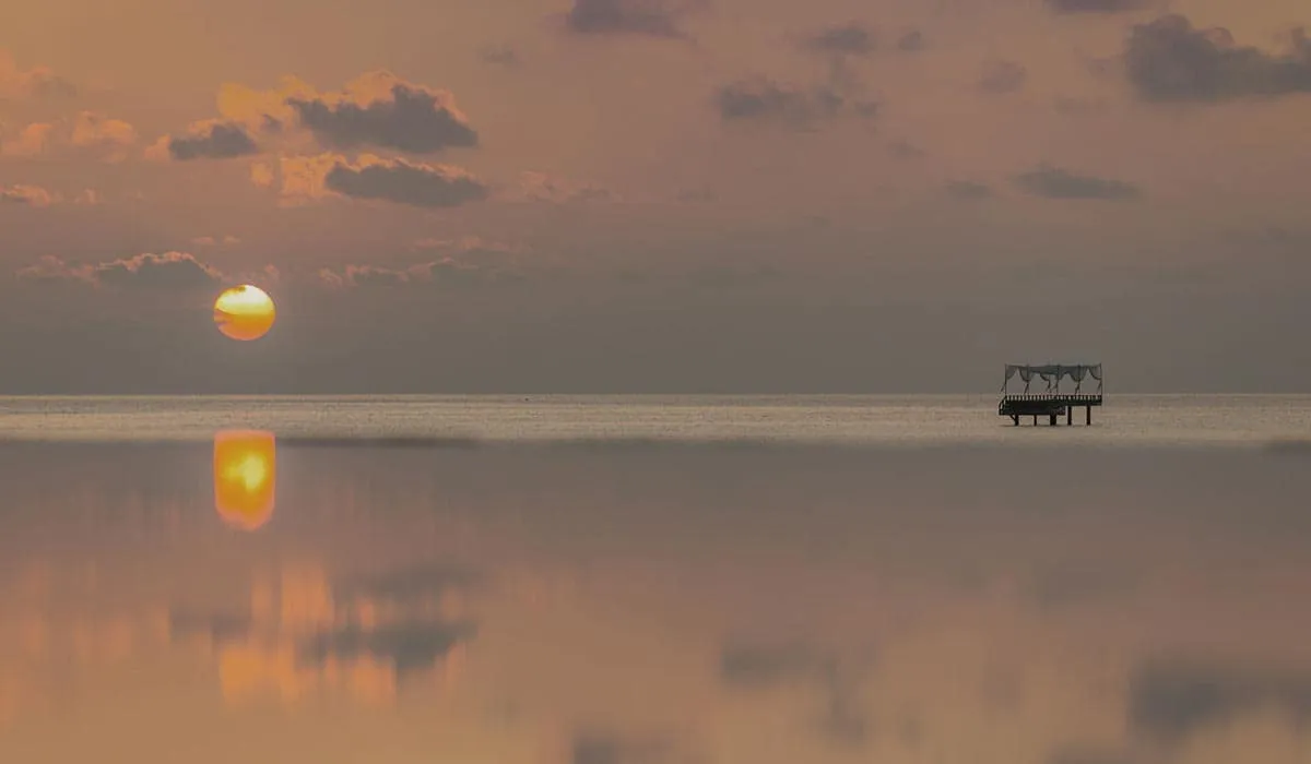 Setting sun reflected in a calm lagoon, with the Piano Deck in the distance