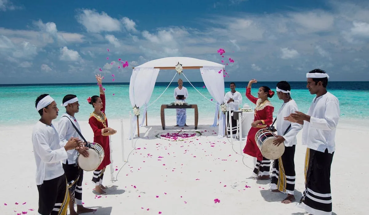 Beach wedding under a white canopy, with traditional drummers and dancers