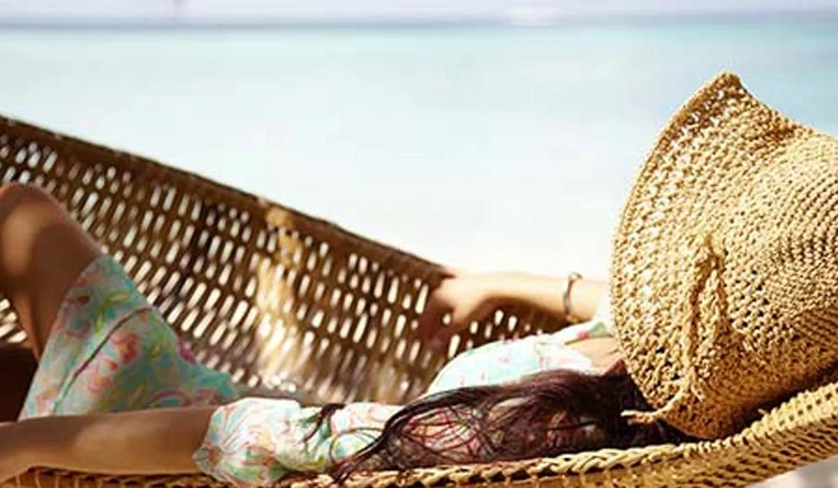 Woman relaxing in a woven hammock, face shaded by a straw hat