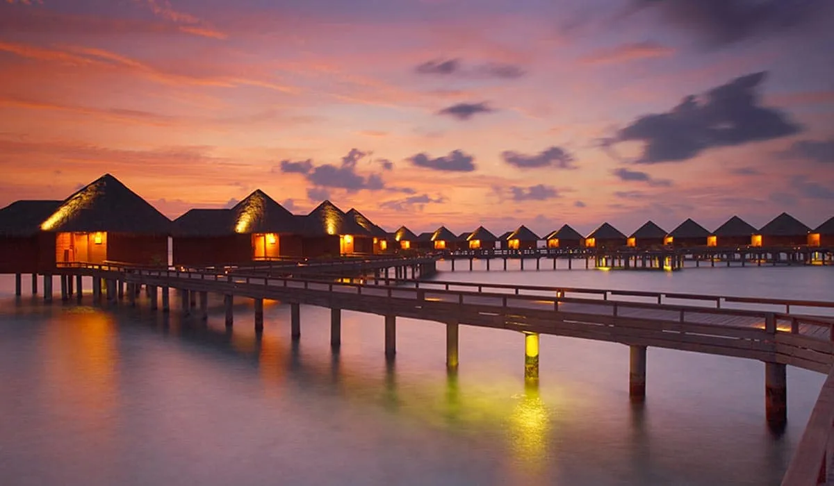 Row of water villas on a lit walkway over the sea at sunset