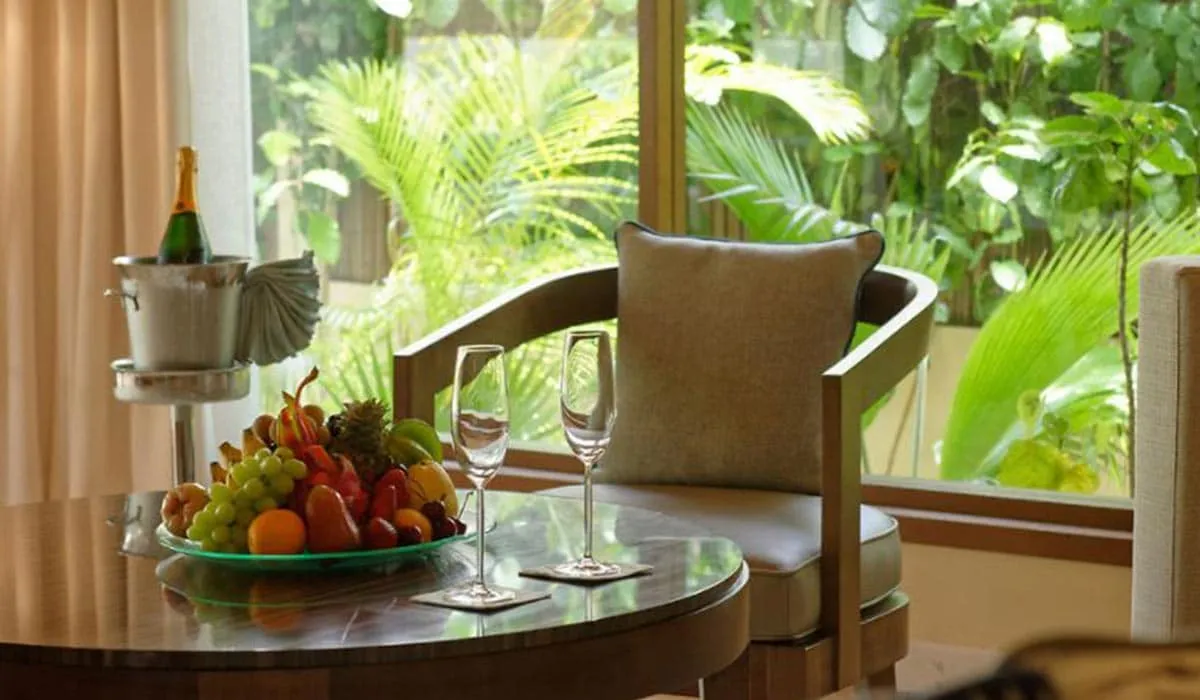 Champagne, fruit bowl and glasses on a table beside a garden-view window