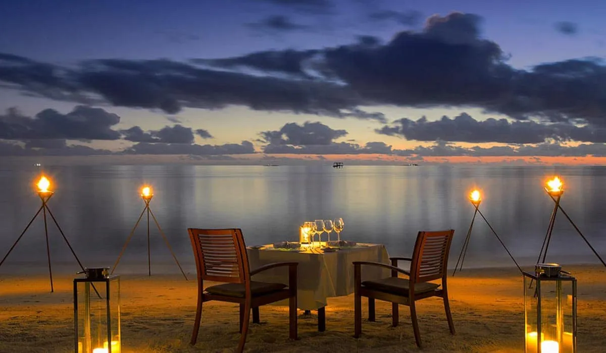 Candlelit dinner table for two on the beach, lit by torches at dusk