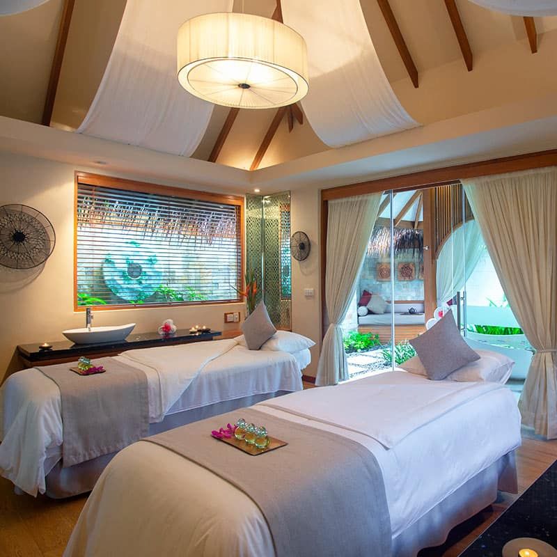 Spa treatment room with two massage beds and a garden-view window