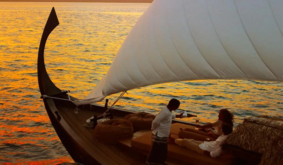 Couple relaxing on a traditional sailing boat at sunset as a crew member serves drinks