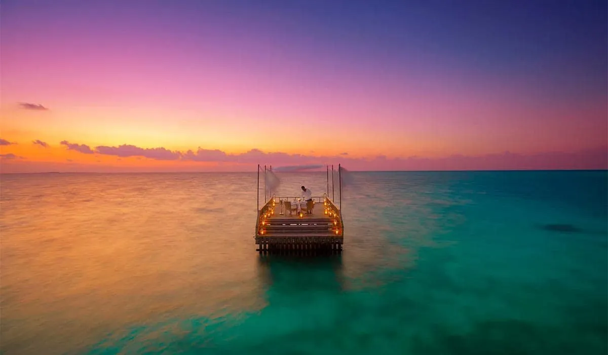 The Piano Deck lit up in the lagoon under a pink sunset sky