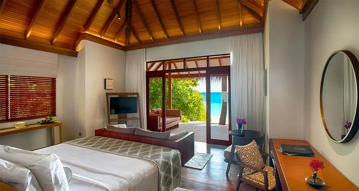 Beach villa bedroom with a timber ceiling and doors opening to the garden and sea