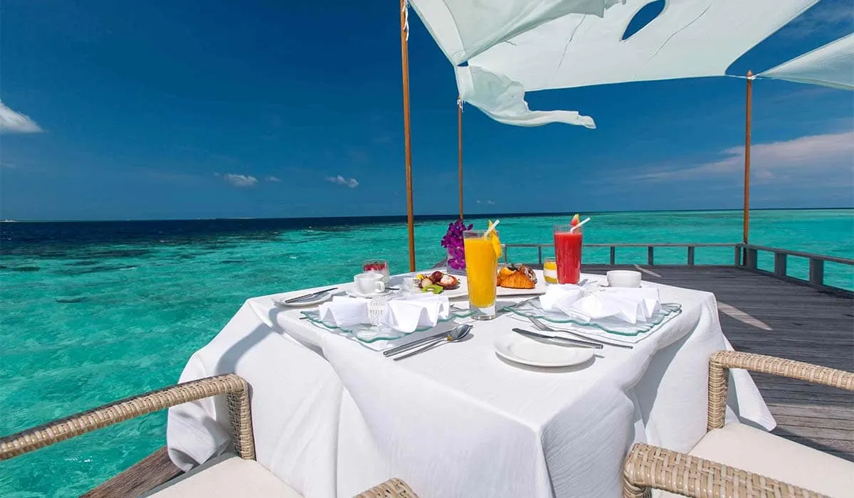 Breakfast table under a white shade sail on a deck overlooking the sea