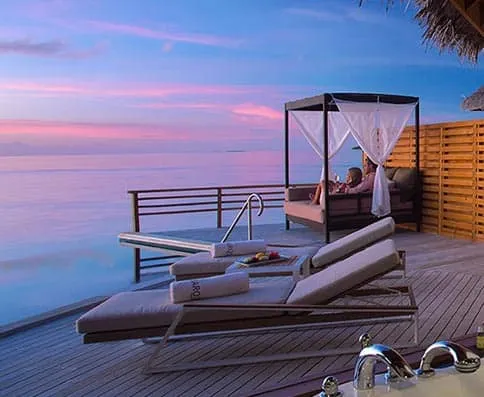 Couple on a curtained daybed on a water villa deck at sunset