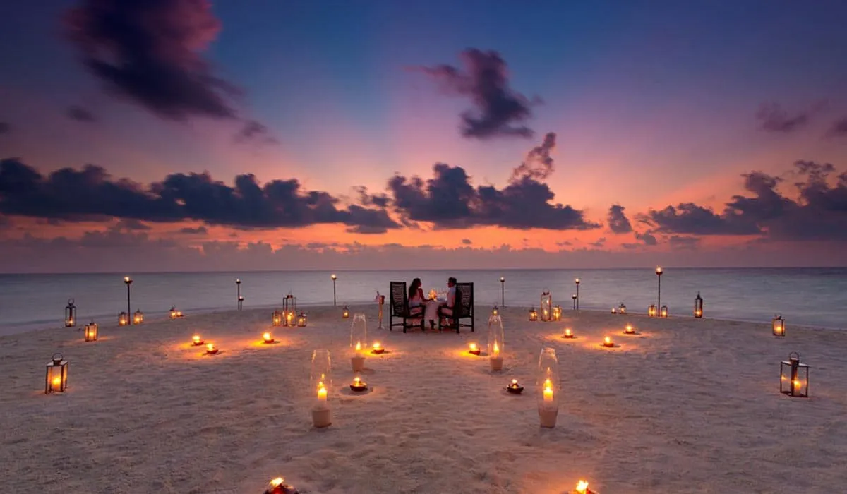 Couple dining on the beach at dusk, surrounded by candles in the sand
