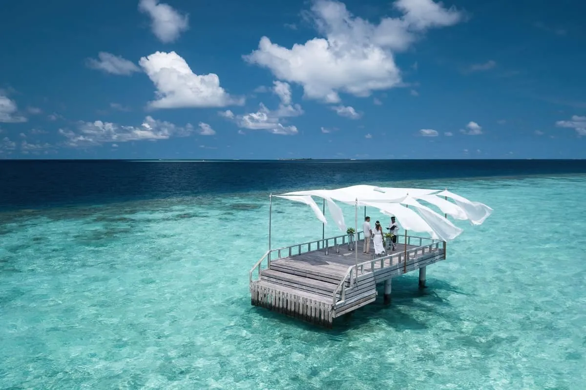 Canopied wooden piano deck standing alone in a turquoise lagoon under a blue sky