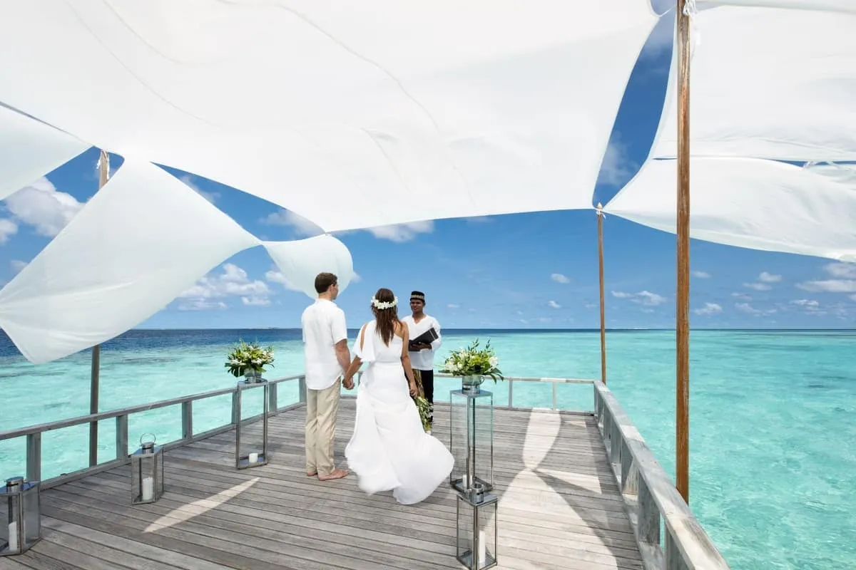 Bride and groom exchanging vows with an officiant on the piano deck under white sail canopies
