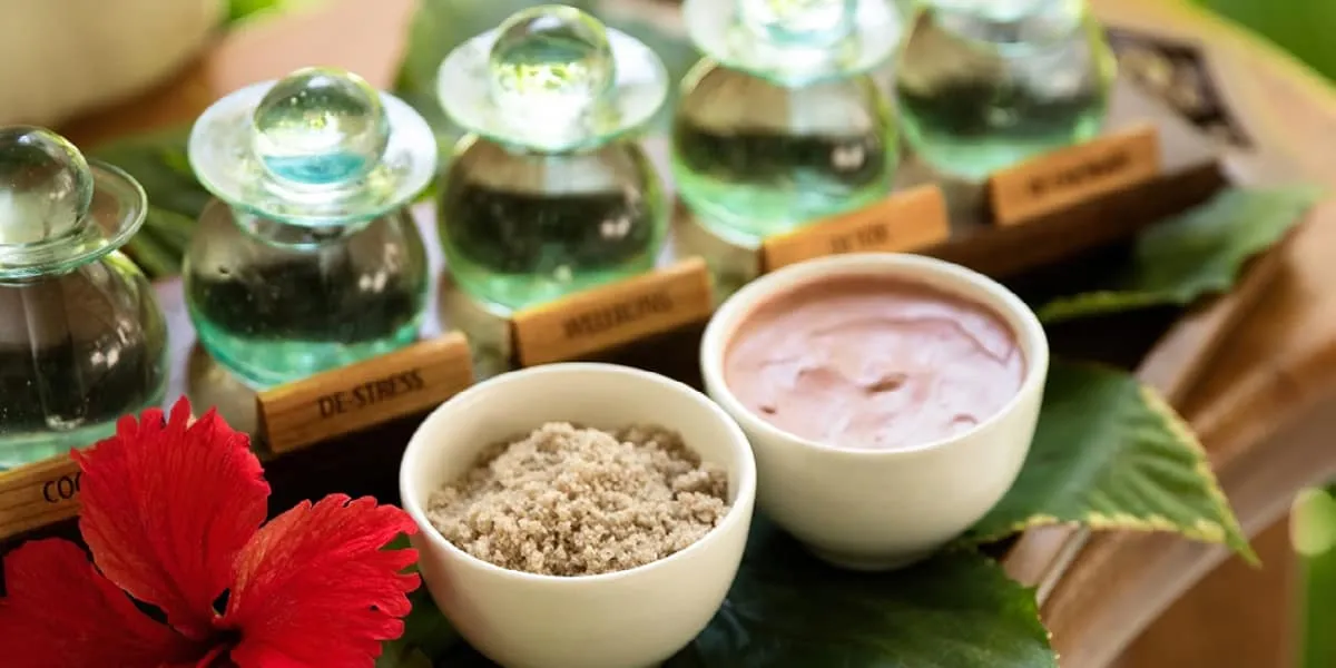 Glass bottles of spa oils with bowls of scrub and a red hibiscus flower