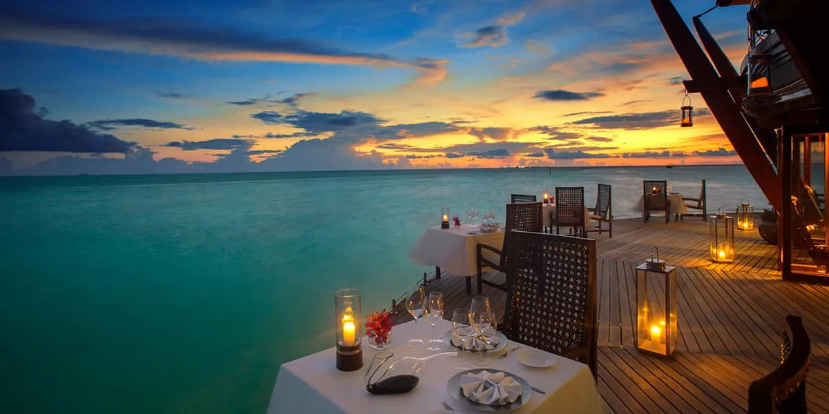 Candlelit table on an overwater restaurant deck at sunset