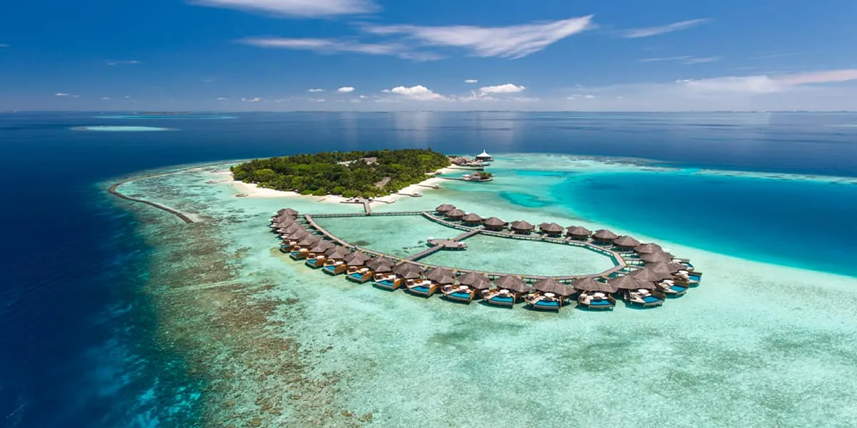 Aerial view of Baros island and its curve of water villas in a turquoise lagoon