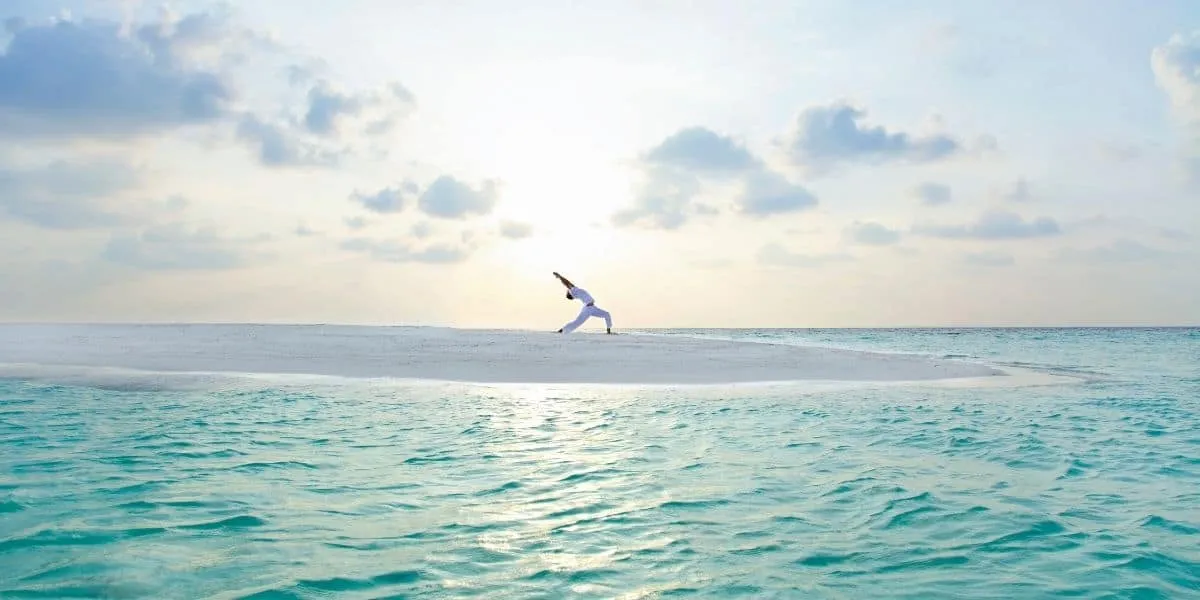 Person holding a yoga pose on a sandbank surrounded by shallow sea