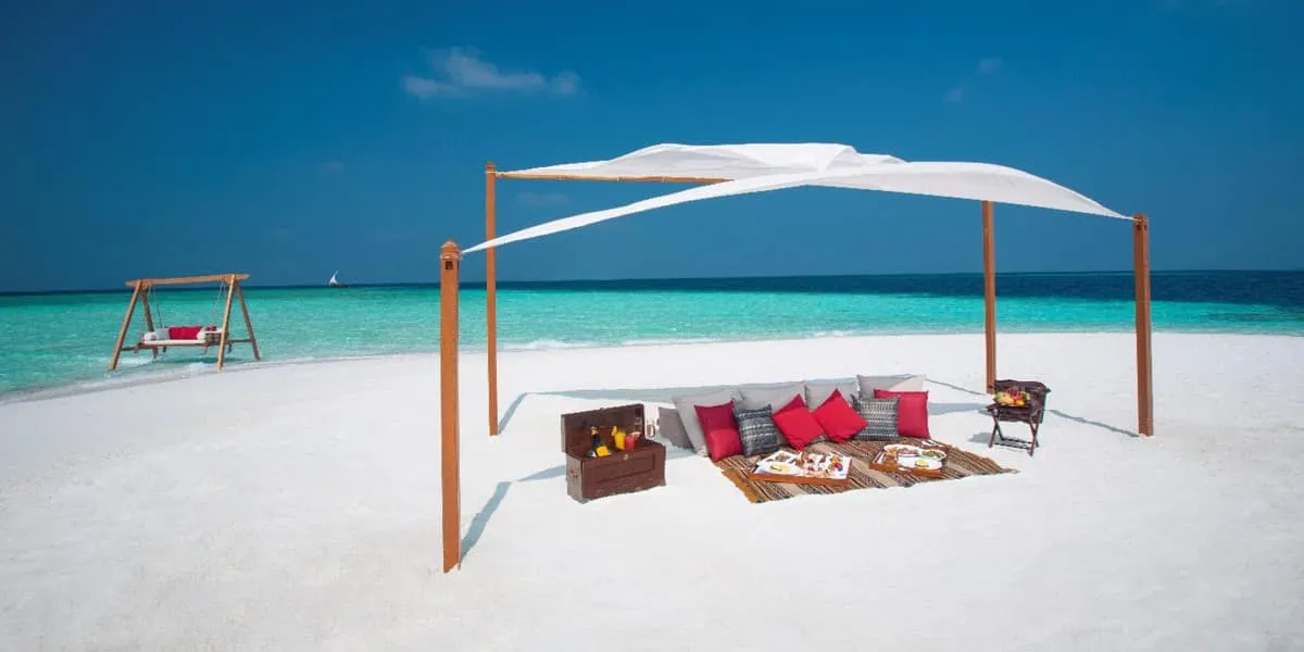 Shaded picnic set-up on a white sand beach, with a swing by the sea