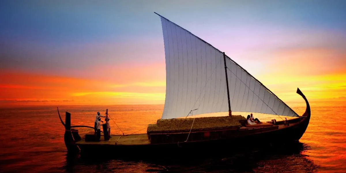 Couple aboard a traditional dhoni with a white sail at sunset