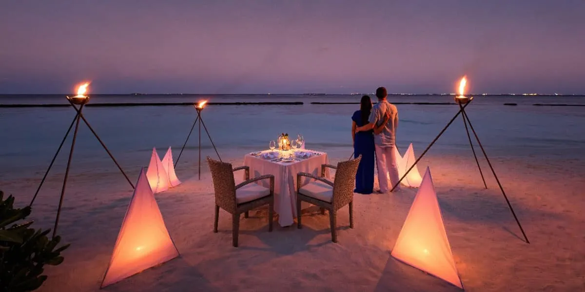 Couple beside a candlelit dinner table on the beach at dusk