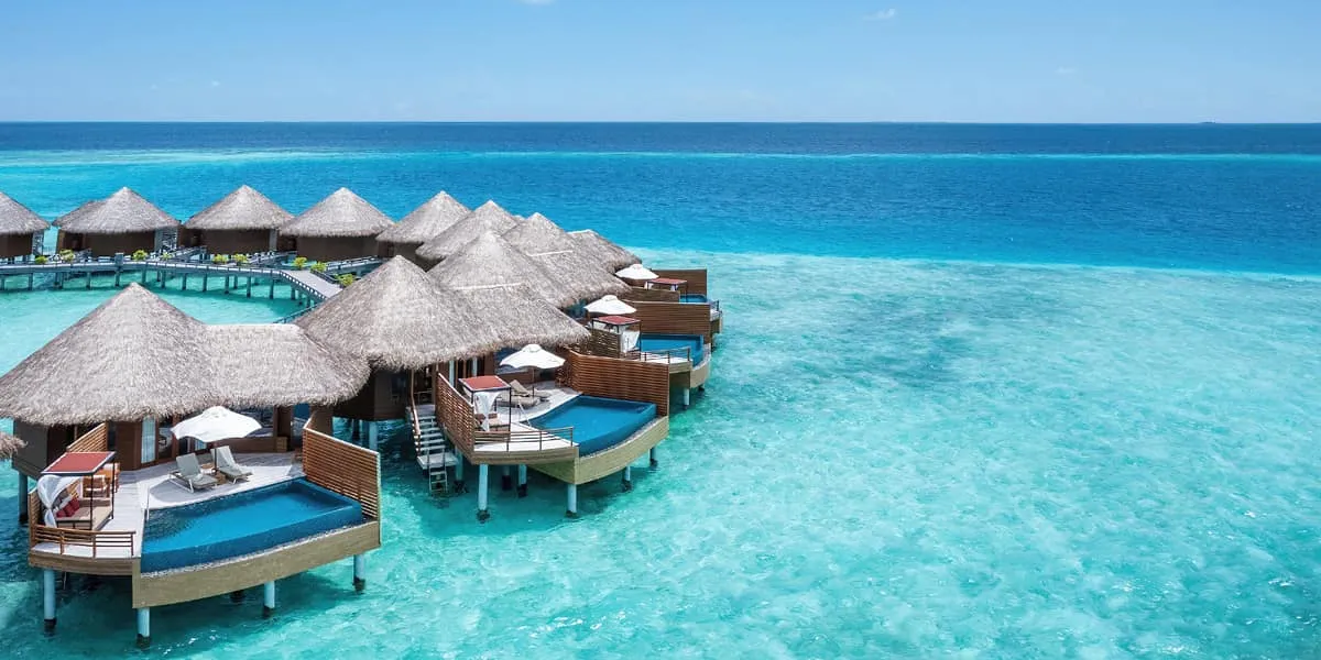 Aerial view of thatched water villas with private pools over the lagoon