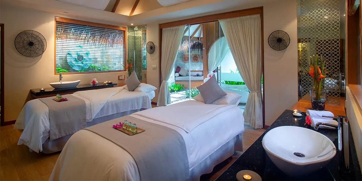 Spa treatment room with two massage beds and a view of the garden