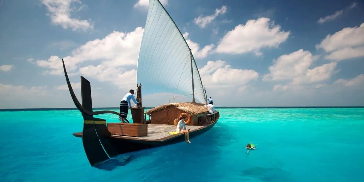 Traditional dhoni moored in a turquoise lagoon with a swimmer nearby